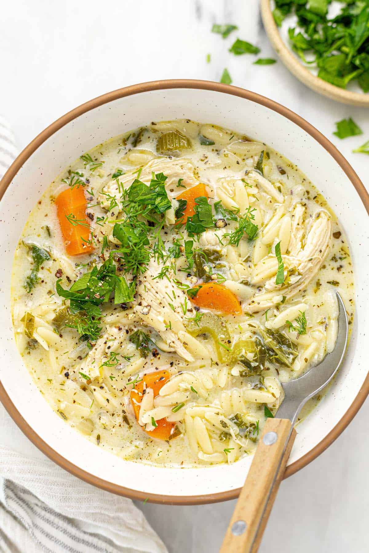 Bowl of lemon chicken orzo soup garnished with fresh herbs. 