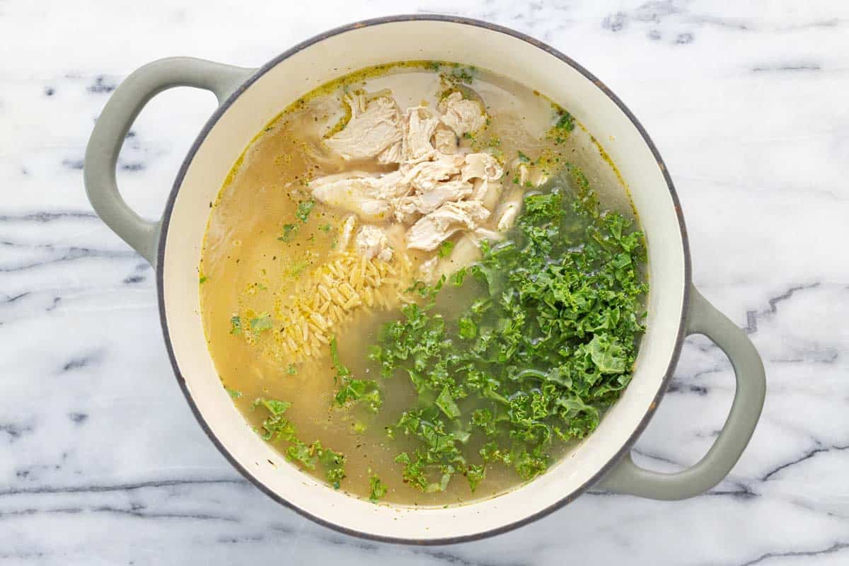 Large soup pot filled with broth, orzo, chicken, and kale. 
