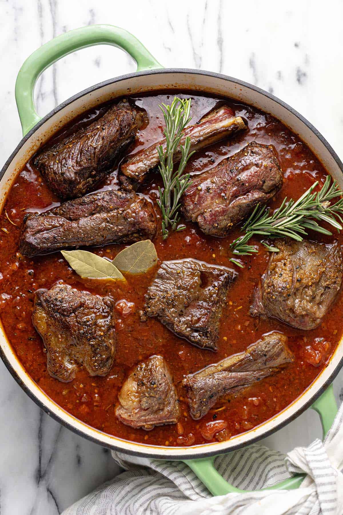 Large pan filled with seared short ribs in a red wine sauce with herbs. 