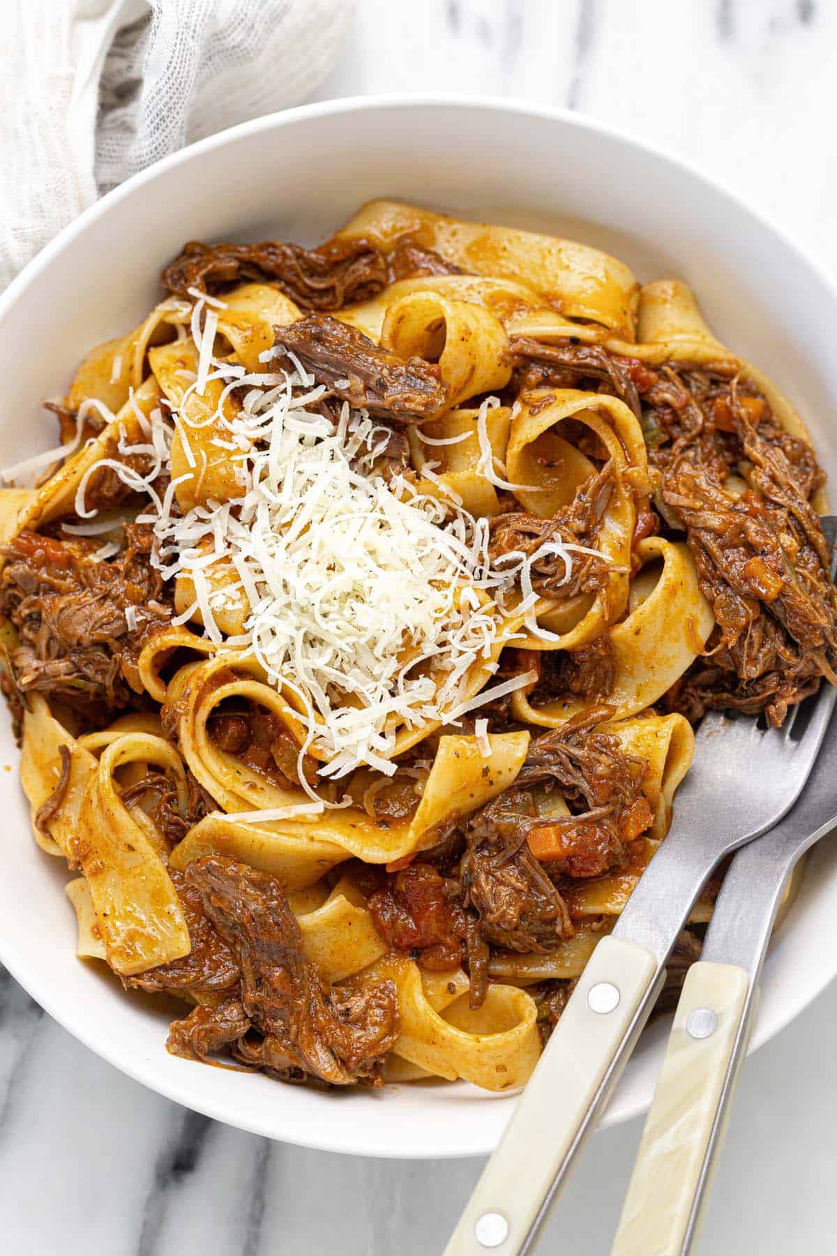 Bowl of pasta tossed in ragu sauce garnished with Parmesan cheese. 