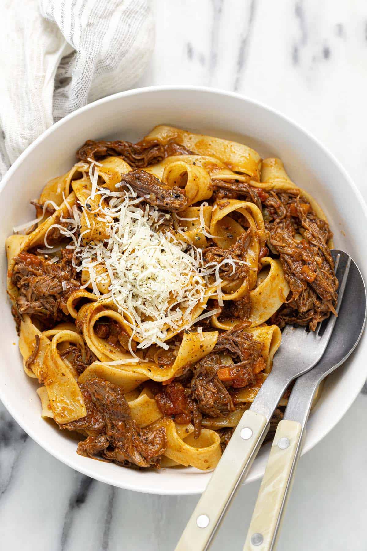 Bowl of pasta tossed in ragu sauce garnished with Parmesan cheese. 