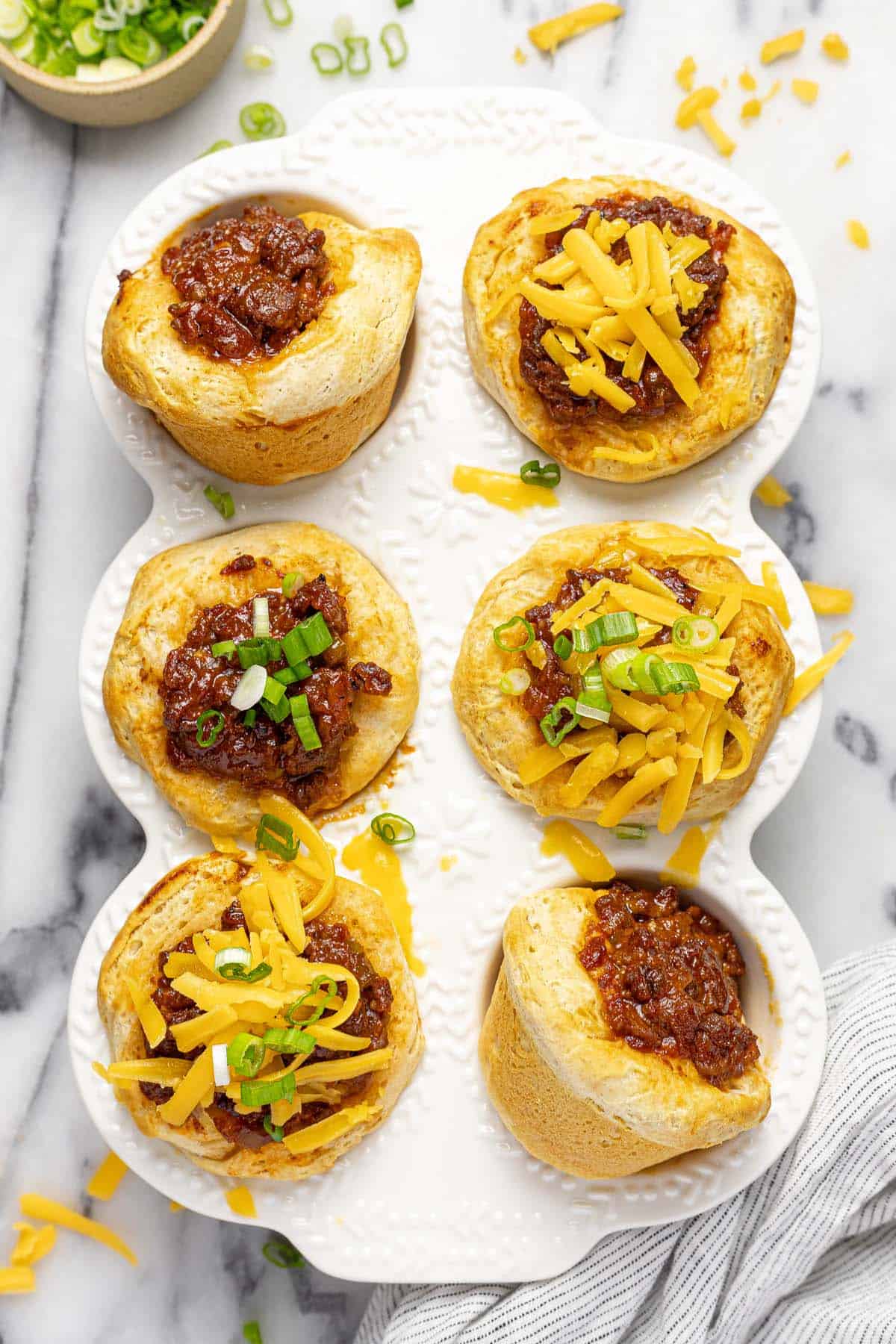 Muffin tin filled with sloppy joe biscuits topped with cheese and green onion. 