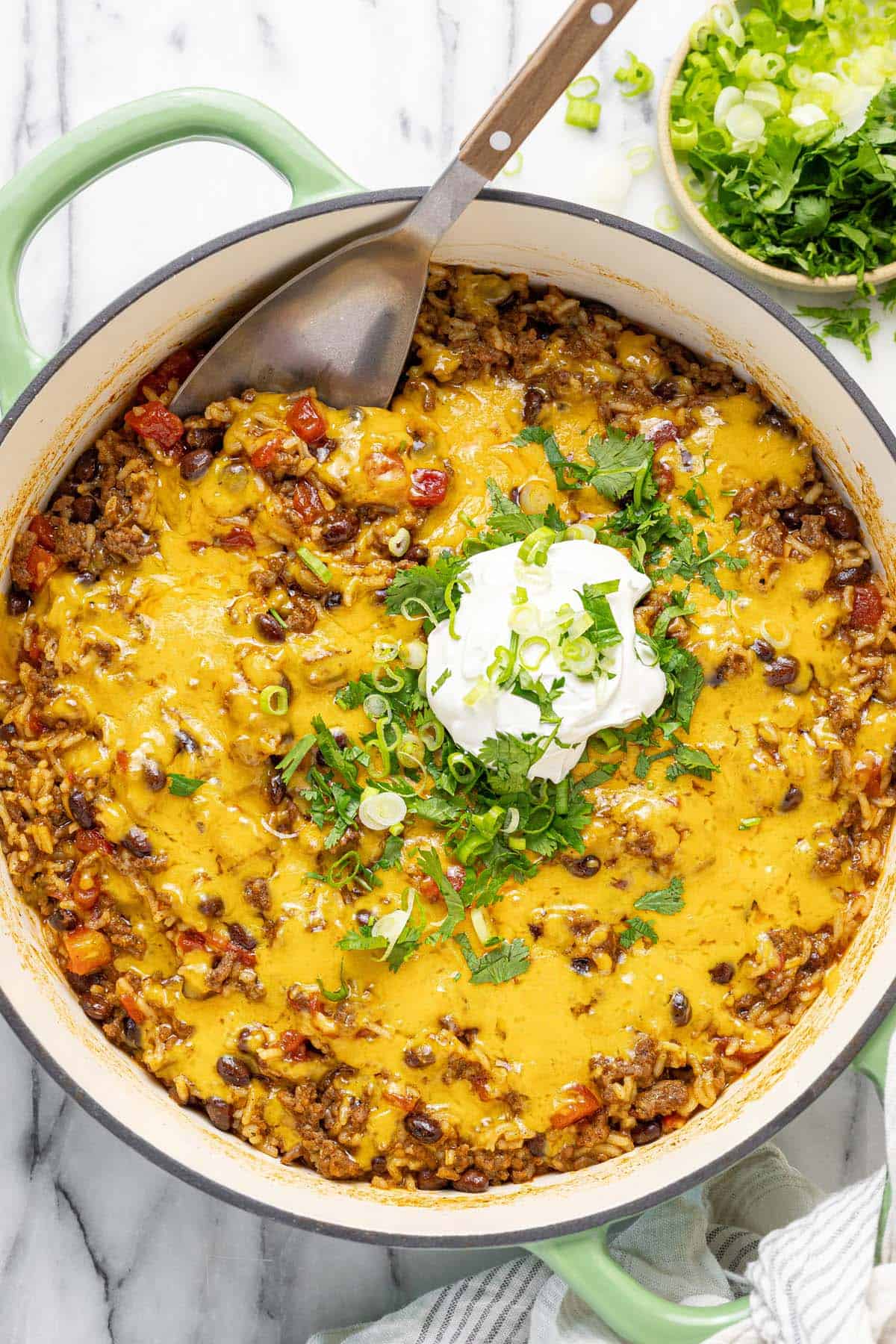 Large pan filled with cheesy ground beef taco rice topped with sour cream and herbs.