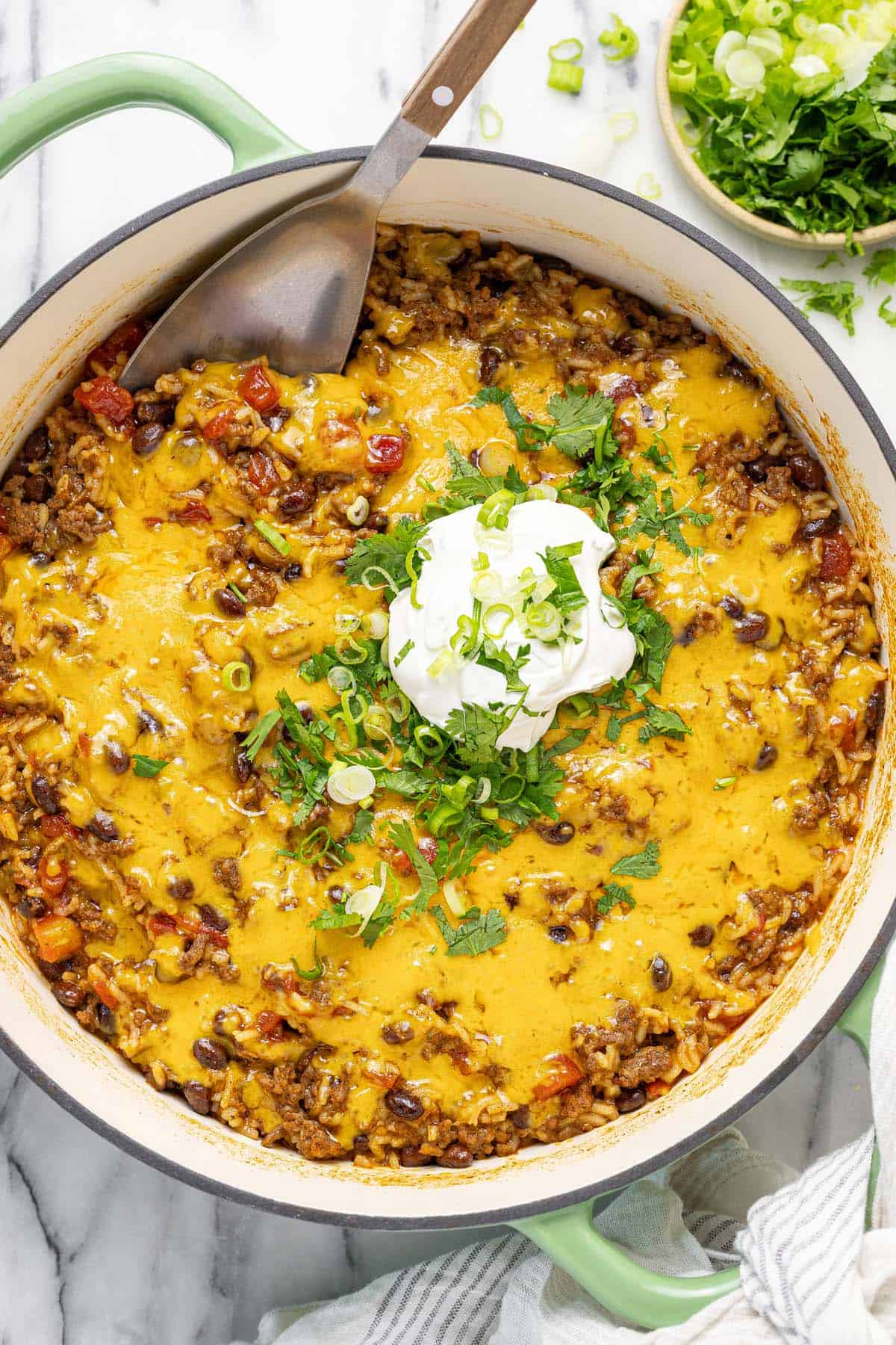 Large pan filled with cheesy ground beef taco rice topped with sour cream and herbs.