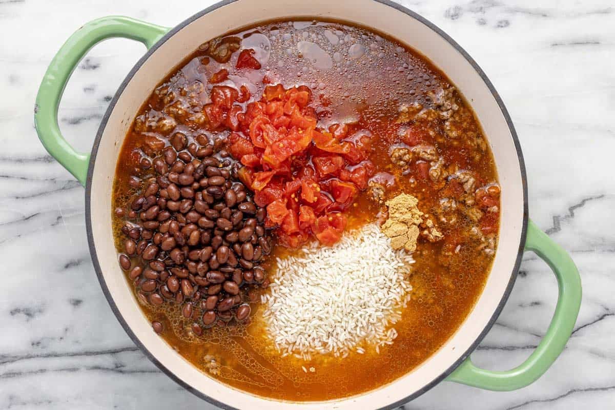 Large pot filled with beans, rice, tomatoes, ground beef, taco seasoning, and broth.