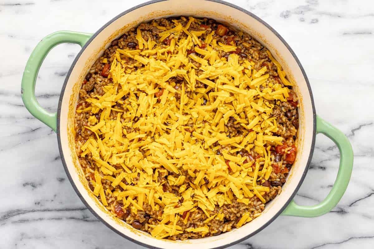 Shredded cheese on top of creamy taco rice in a large pan.