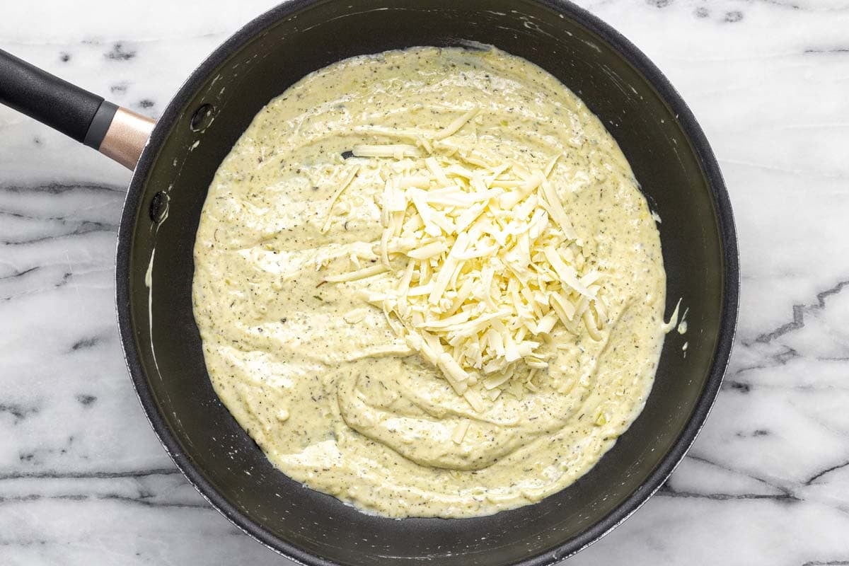 Creamy au gratin sauce with shredded cheese on top in a pan.