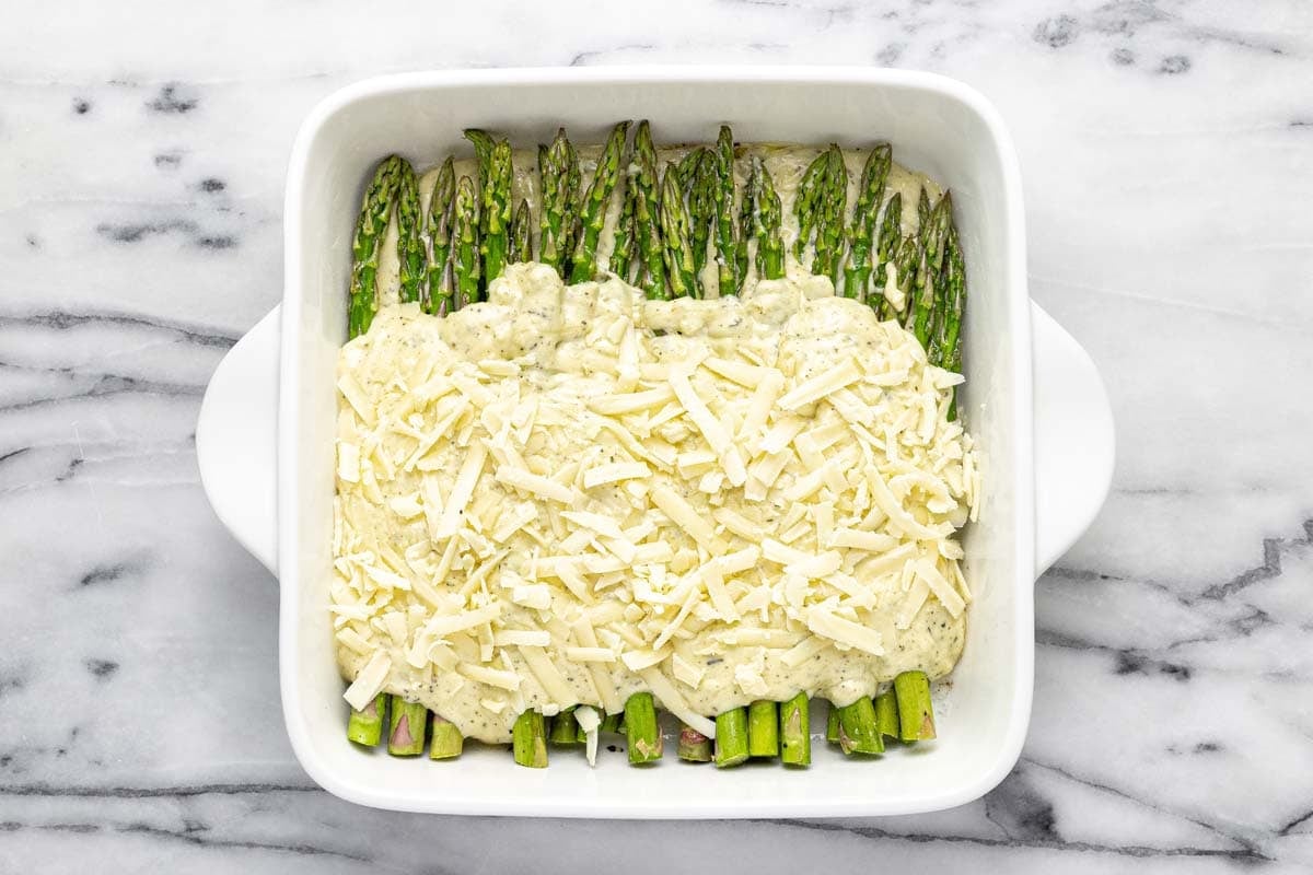 Asparagus in a baking dish with creamy sauce and shredded cheese on top.