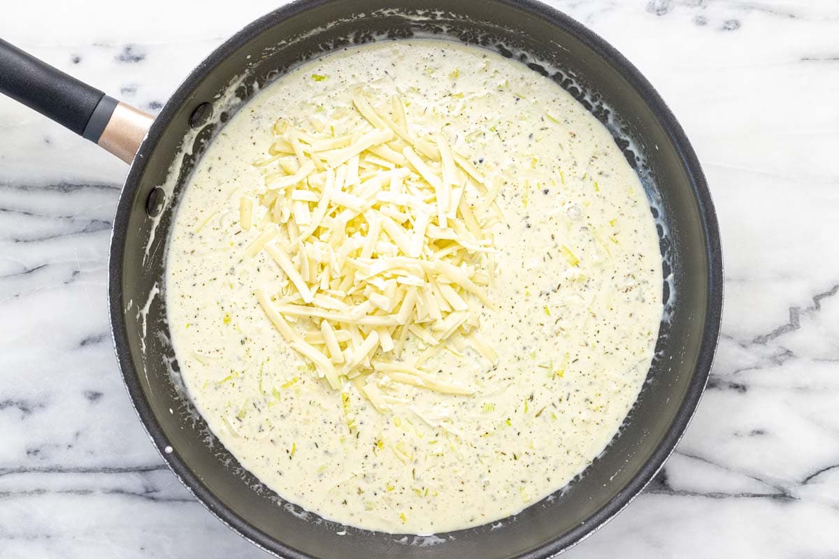 Creamy sauce with shredded cheese in a large pan. 