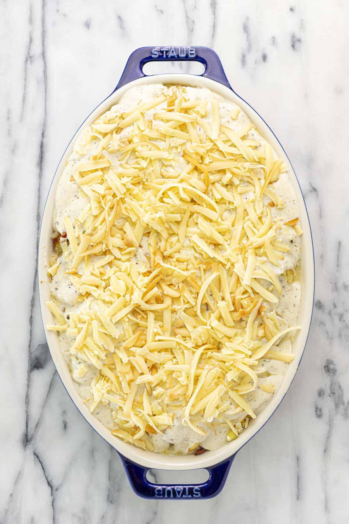 Shredded cheese on top of au gratin potatoes in a baking dish. 