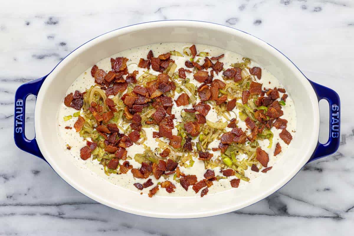 A casserole dish with cheesy sauce, bacon, and leeks. 