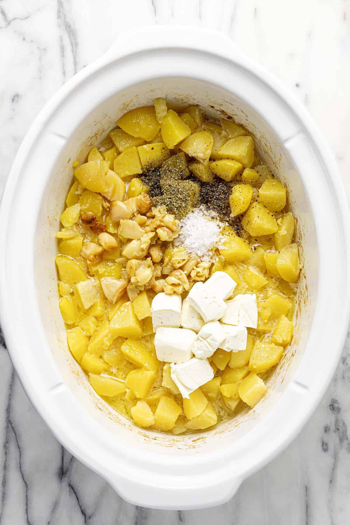 Diced potatoes in a crock pot with roasted garlic, herbs, and cream cheese. 