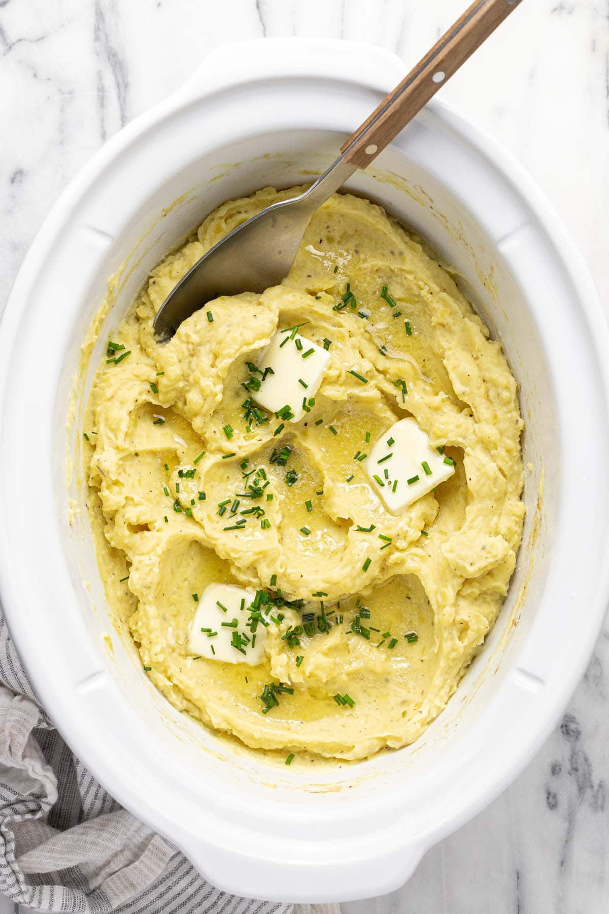 Crock pot insert filled with creamy homemade mashed potatoes garnished with butter and chives. 