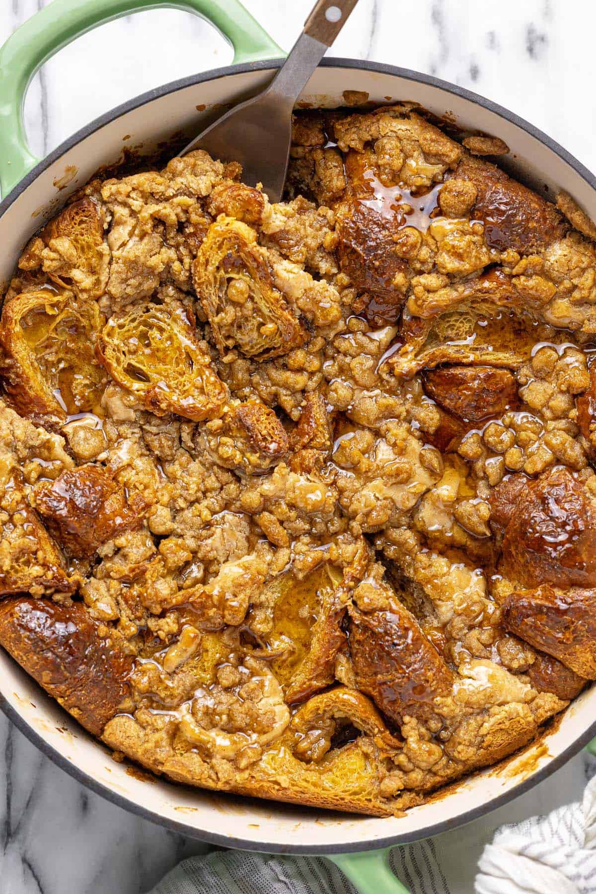 Freshly baked croissant French toast bake in a large pan topped with syrup.