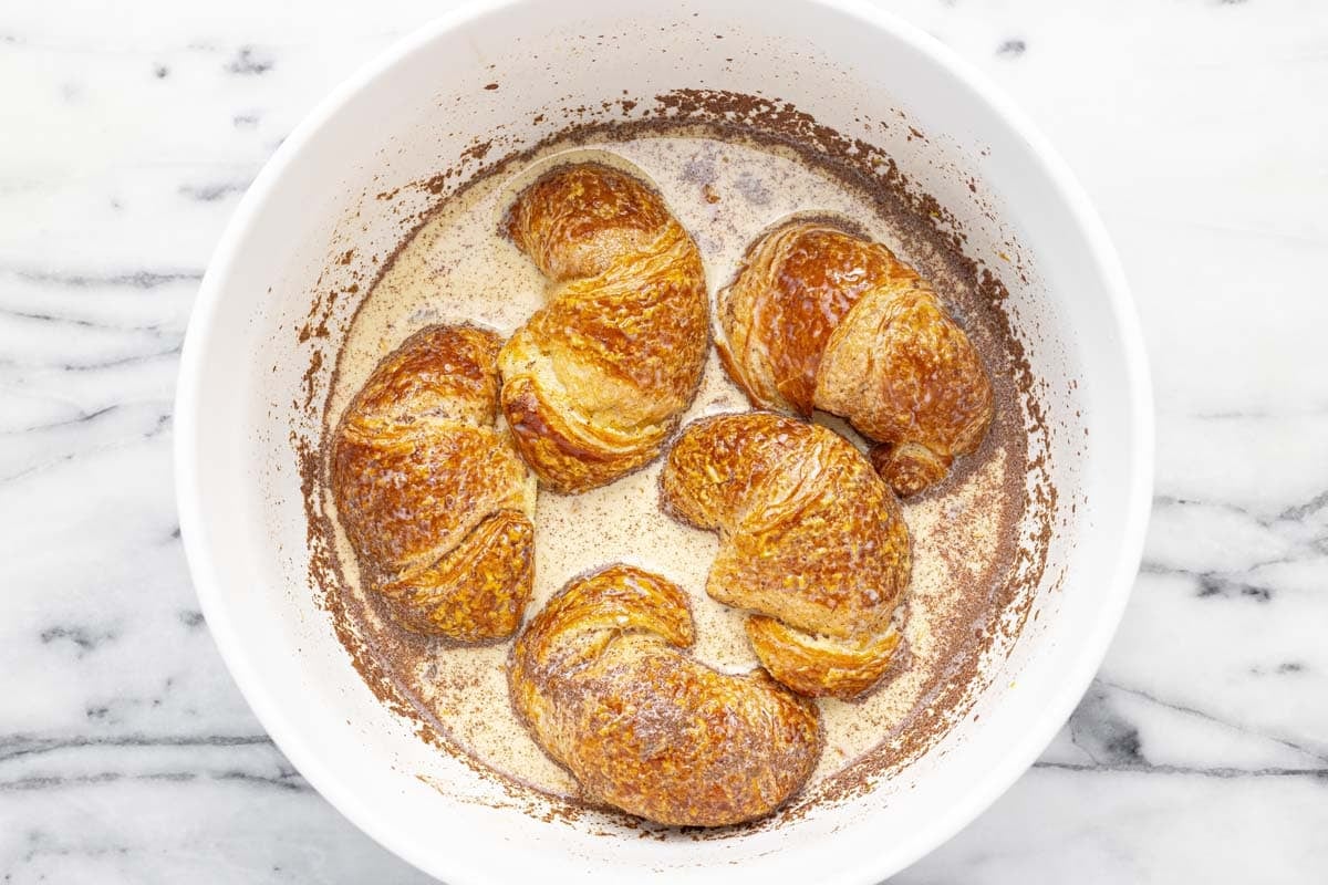 Bowl of French toast batter with croissants soaking in it.