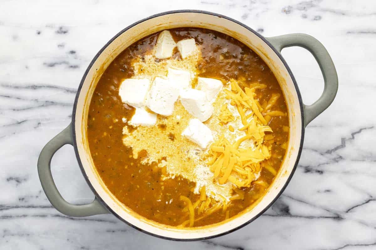 Cheese, half and half, and cream cheese added to a large pot of soup. 