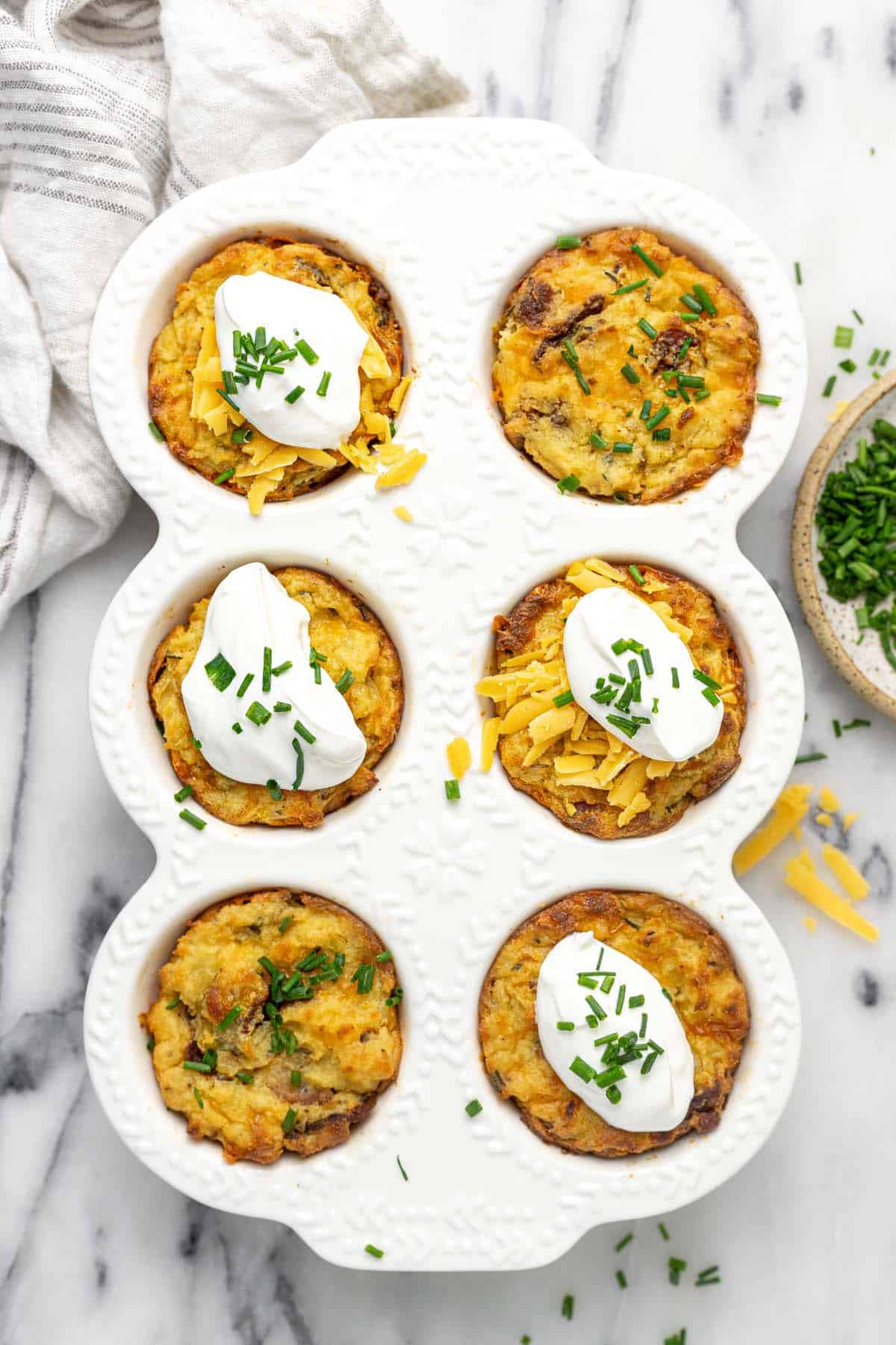 Muffin pan filled with mashed potato muffins garnished with sour cream and chives. 