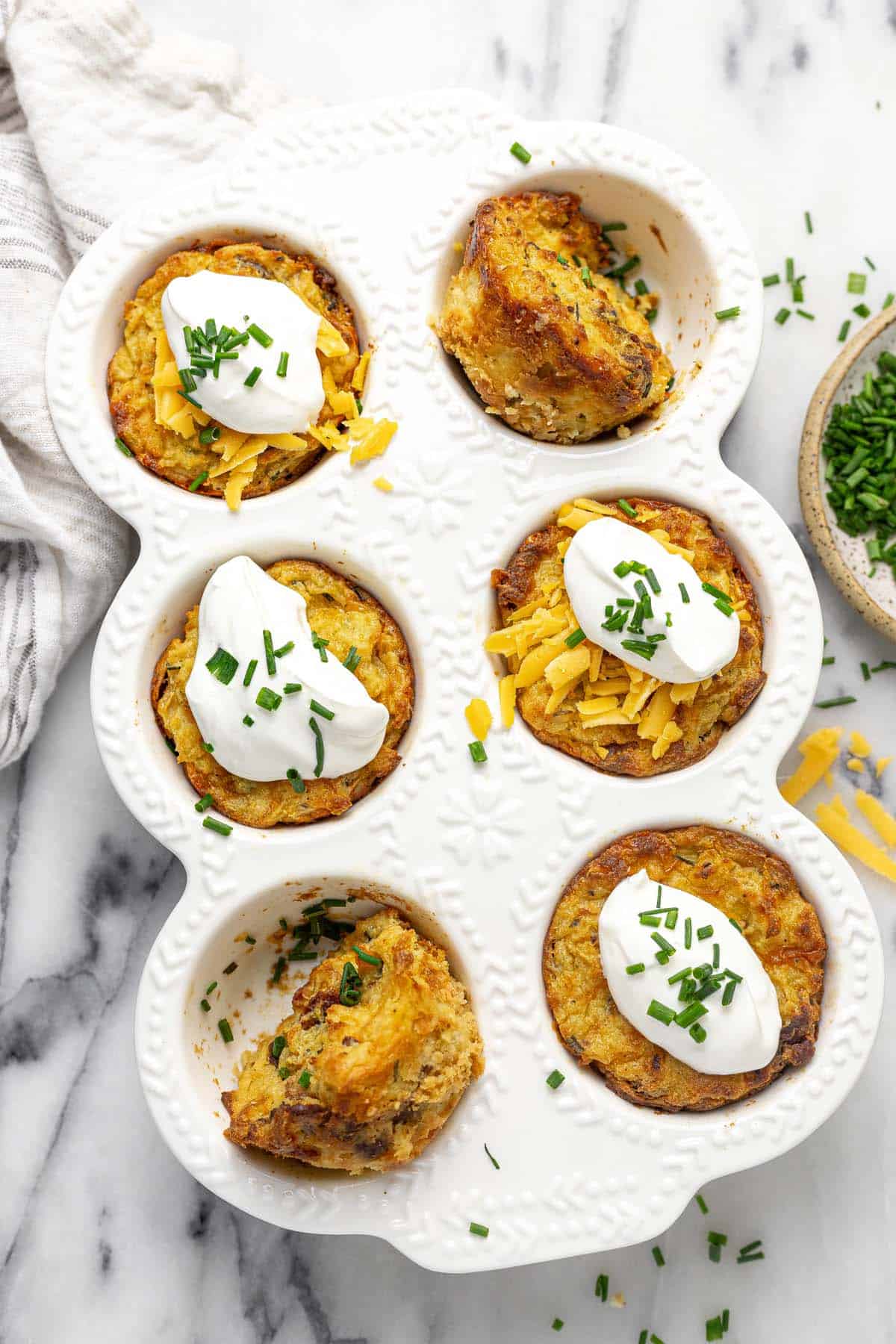 Muffin pan filled with mashed potato muffins garnished with sour cream and chives. 
