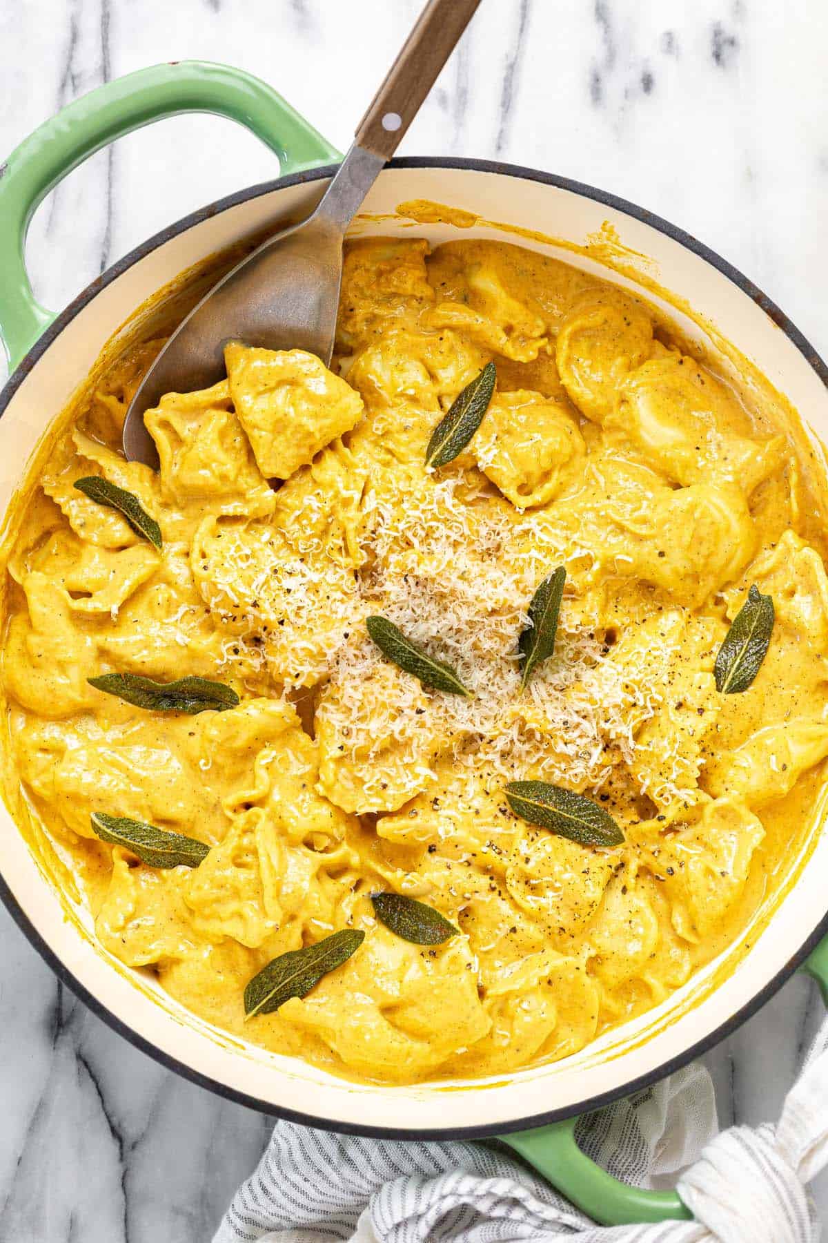 Large pan filled with pumpkin tortellini garnished with fried sage and Parmesan. 