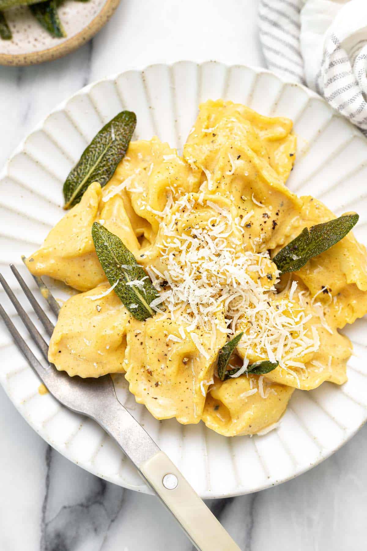 Plate with pumpkin tortellini and fried sage topped with Parmesan. 