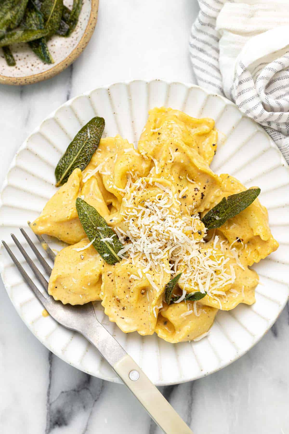 Plate with pumpkin tortellini and fried sage topped with Parmesan. 