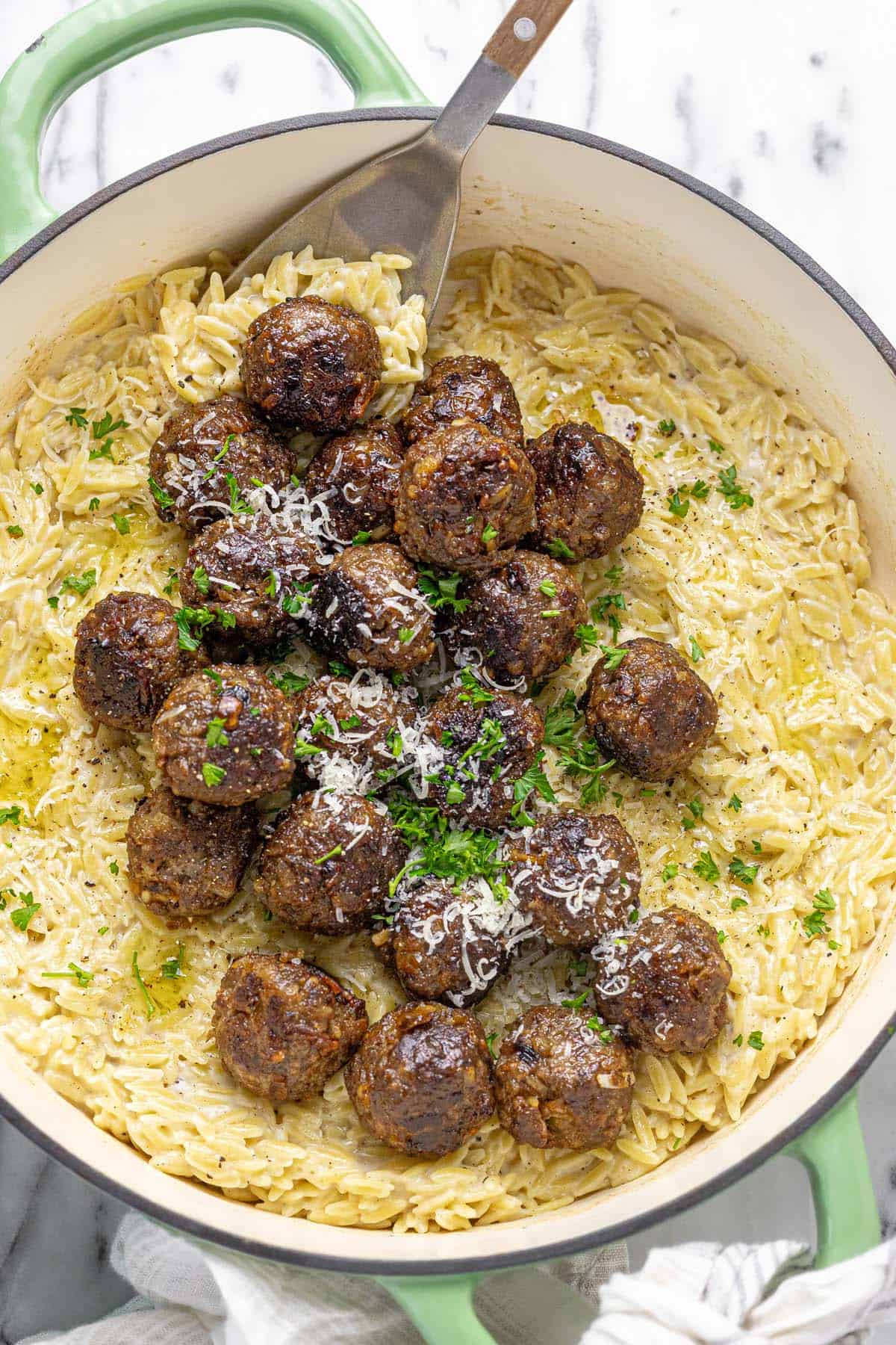Pan seared meatballs in a pan of cheesy orzo pasta.