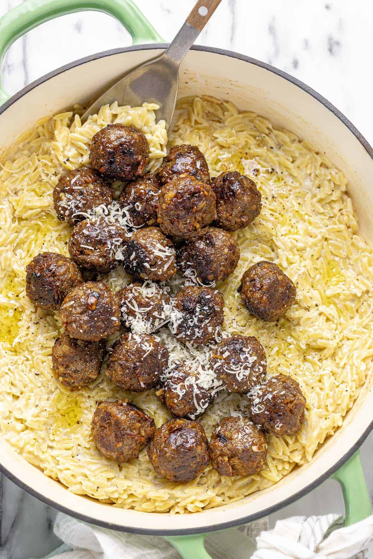 French onion meatballs in a pan of cheesy orzo topped with Parmesan cheese.