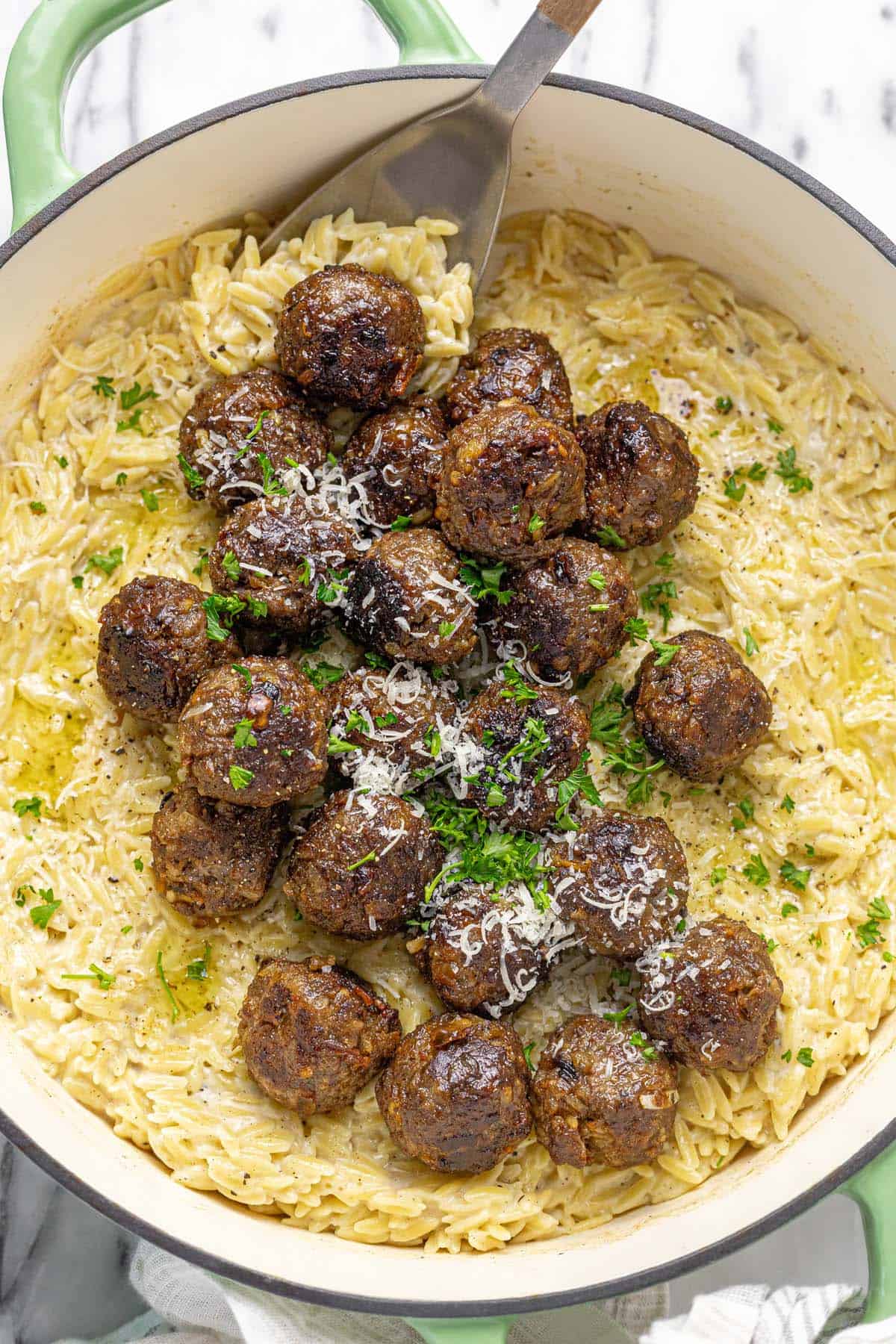 Large pan filled with French onion meatballs and cheesy orzo topped with Parmesan and parsley.
