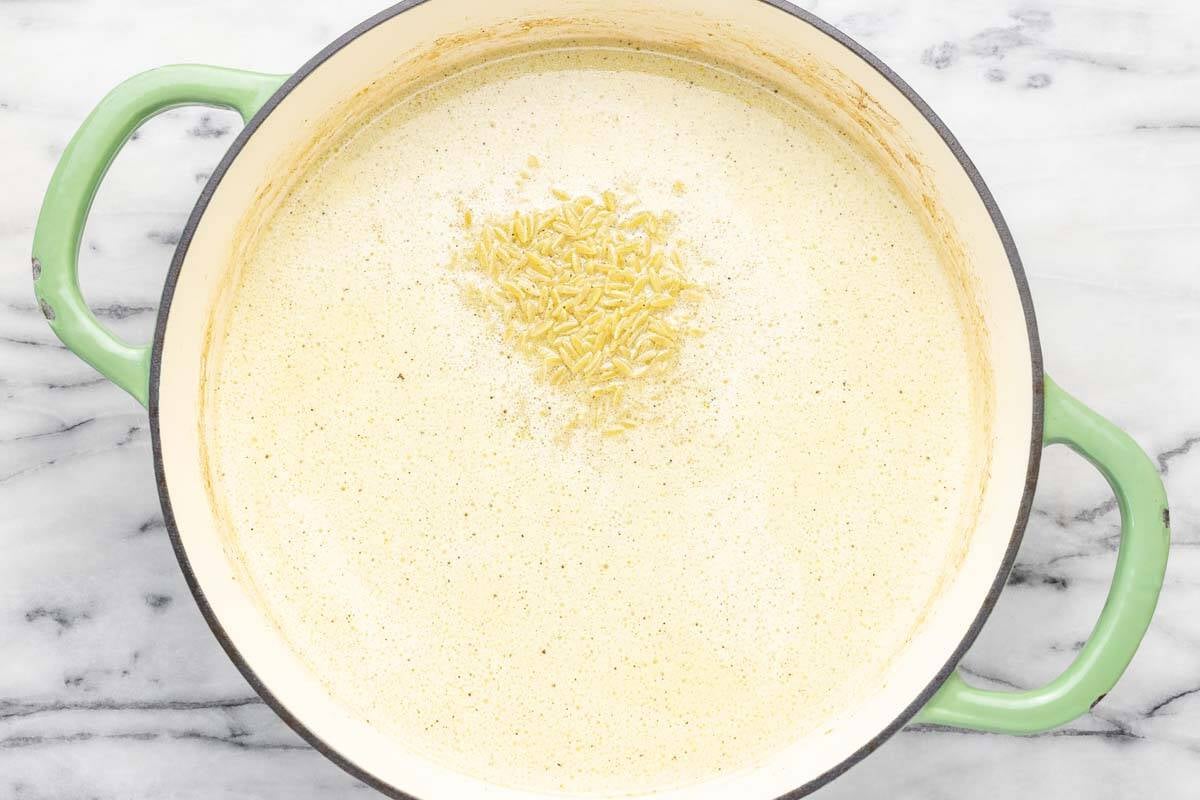Orzo, cream, and broth in a large pan.