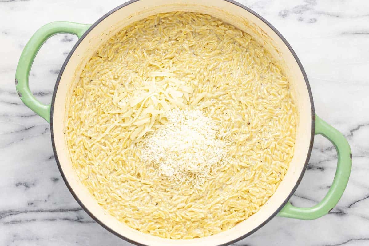 Large pan of creamy orzo with shredded cheese added on top.