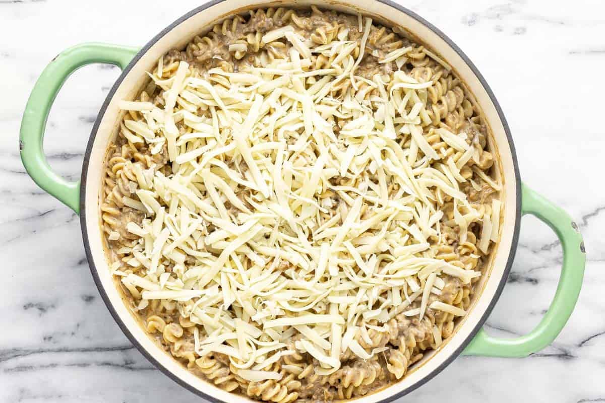 Creamy French onion pasta in a large pan with shredded cheese on top.