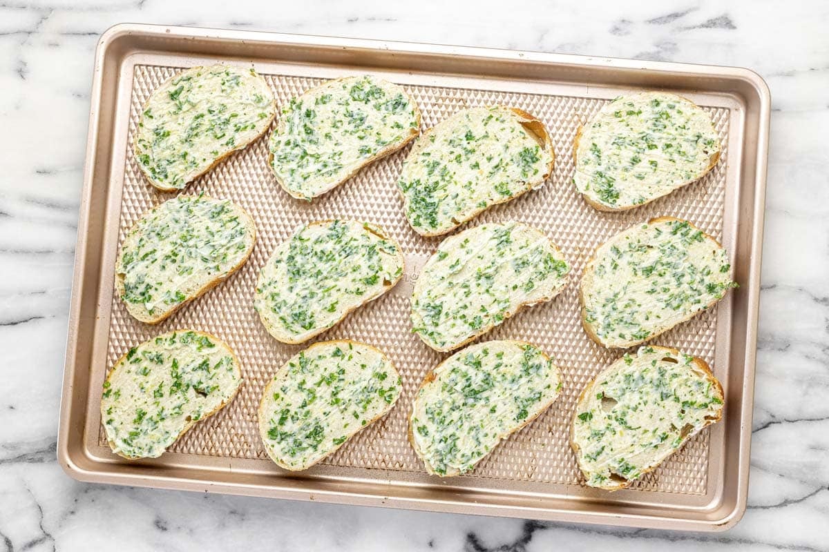 Baking sheet with sliced French bread spread with garlic butter.