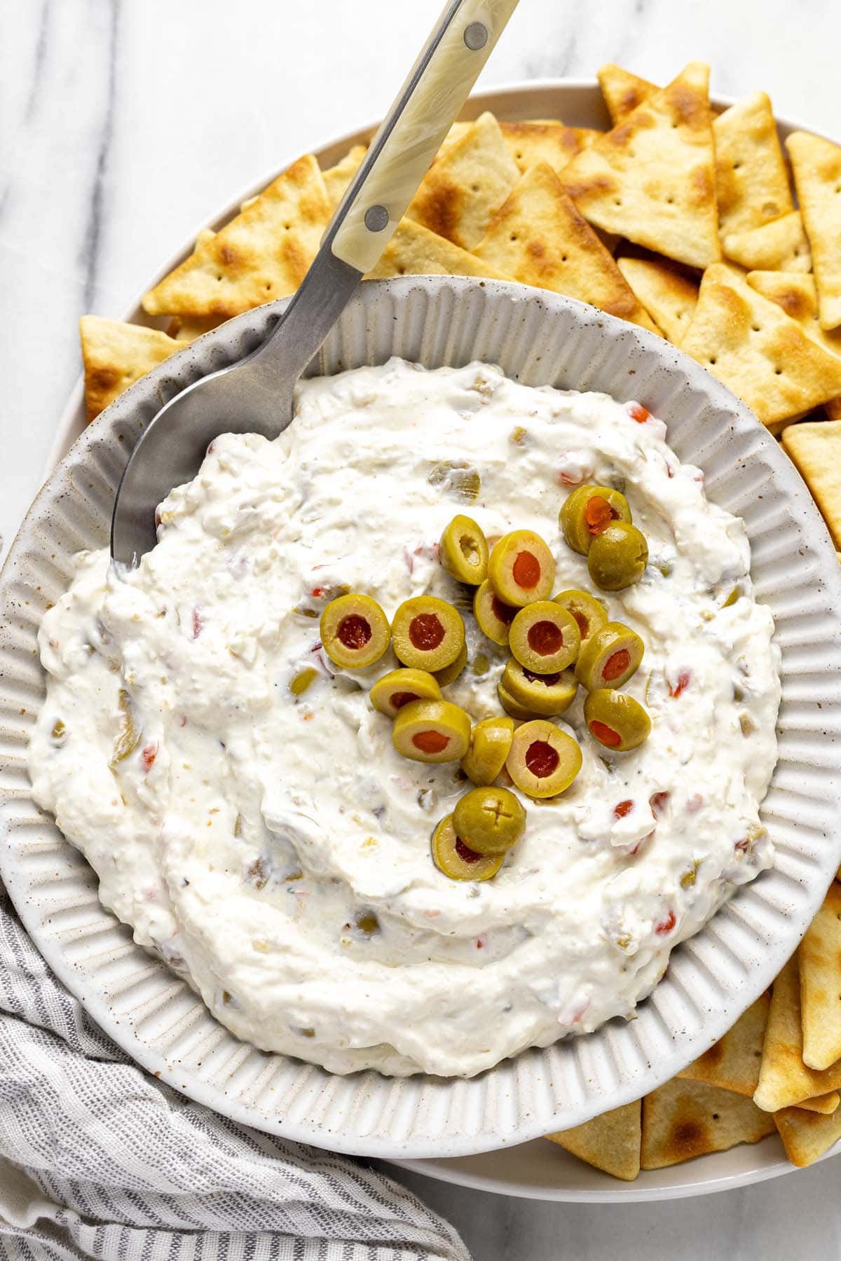 Bowl of homemade olive dip on a plate of pita chips. 