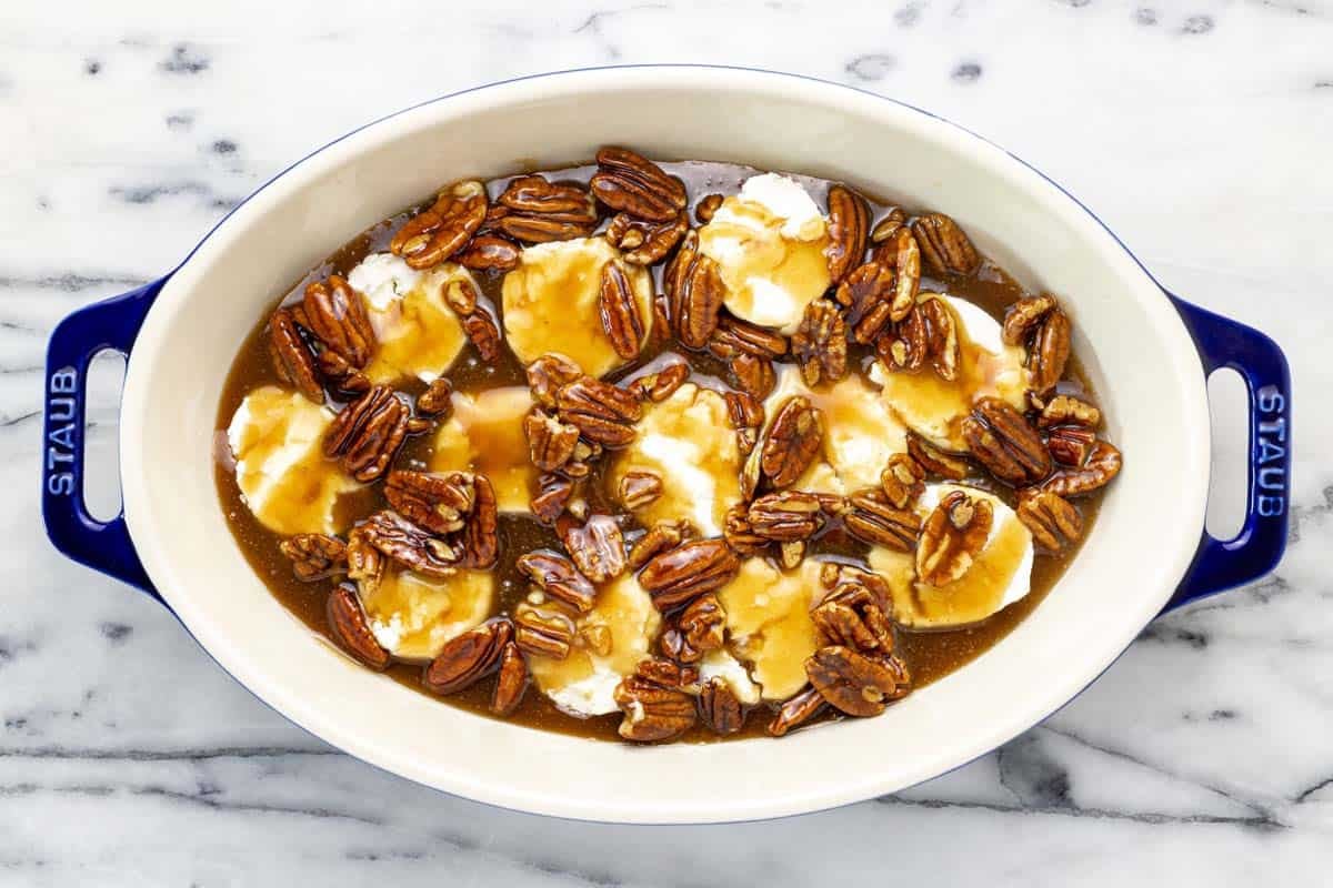 Sliced goat cheese topped with pecan pie caramel in a baking dish.