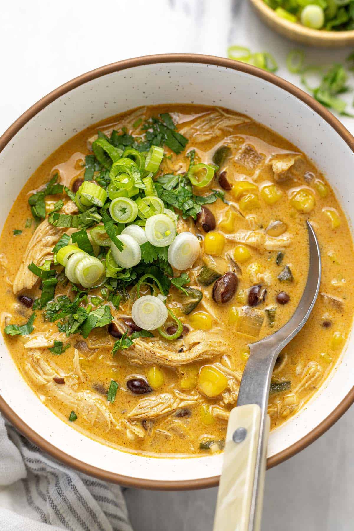 Bowl of creamy chicken poblano soup garnished with green onion and cilantro.