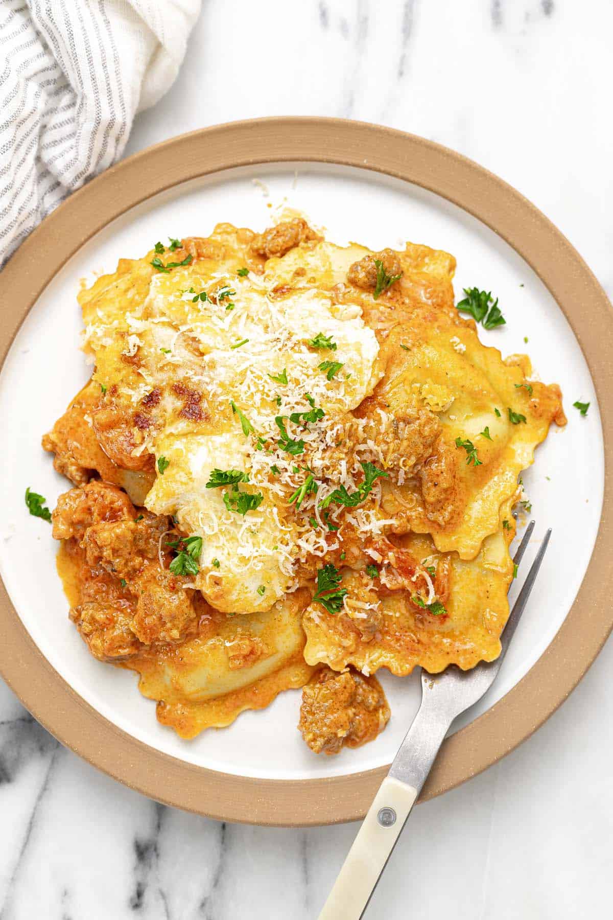 Creamy sausage ravioli on a plate garnished with Parmesan and parsley.