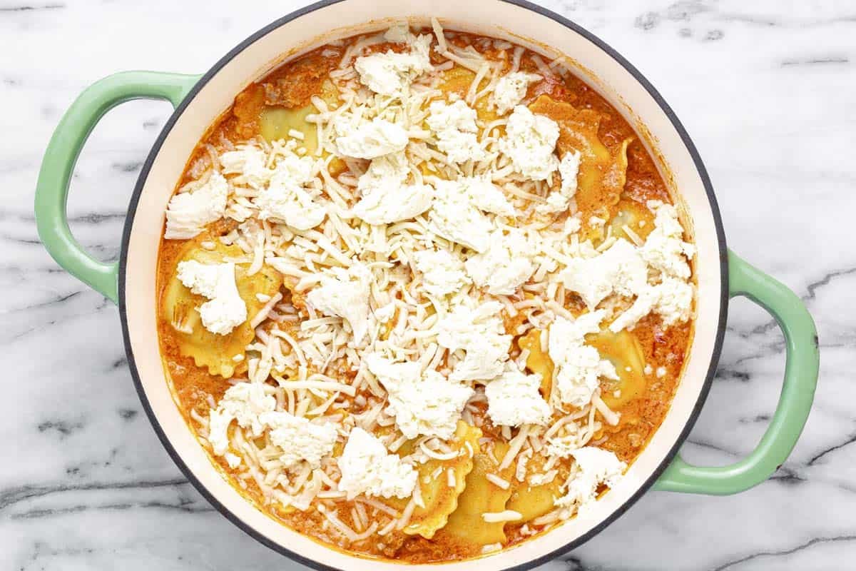 Fresh mozzarella and shredded cheese on top of a pan of ravioli.