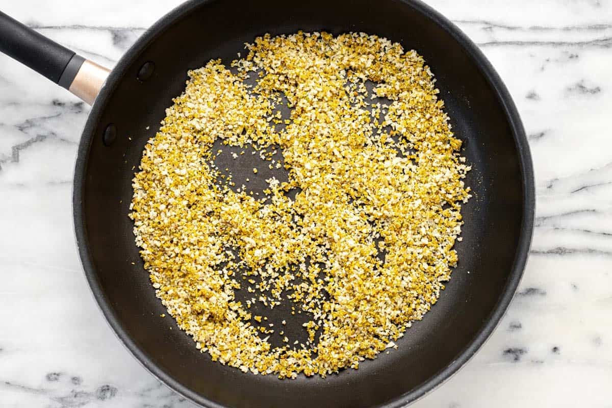 Large pan filled with breadcrumbs, pistachios, and olive oil mixed together.