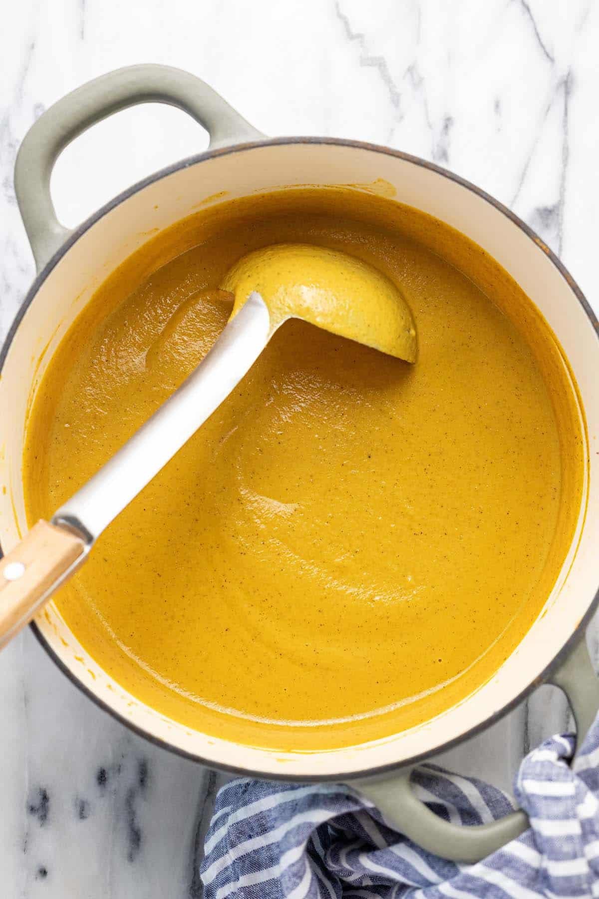 Creamy cauliflower and carrot soup in a large pot with a ladle.