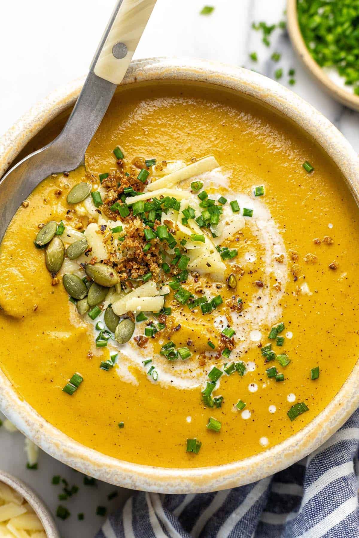 Bowl filled with creamy cauliflower soup garnished with cheese, pumpkin seeds, and breadcrumbs.