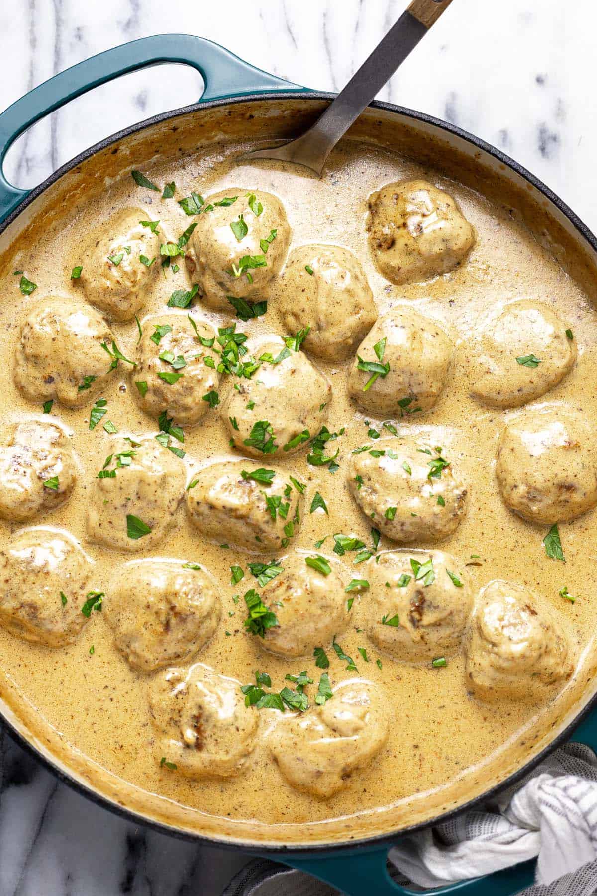 Large pan filled with creamy Swedish meatballs garnished with parsley. 