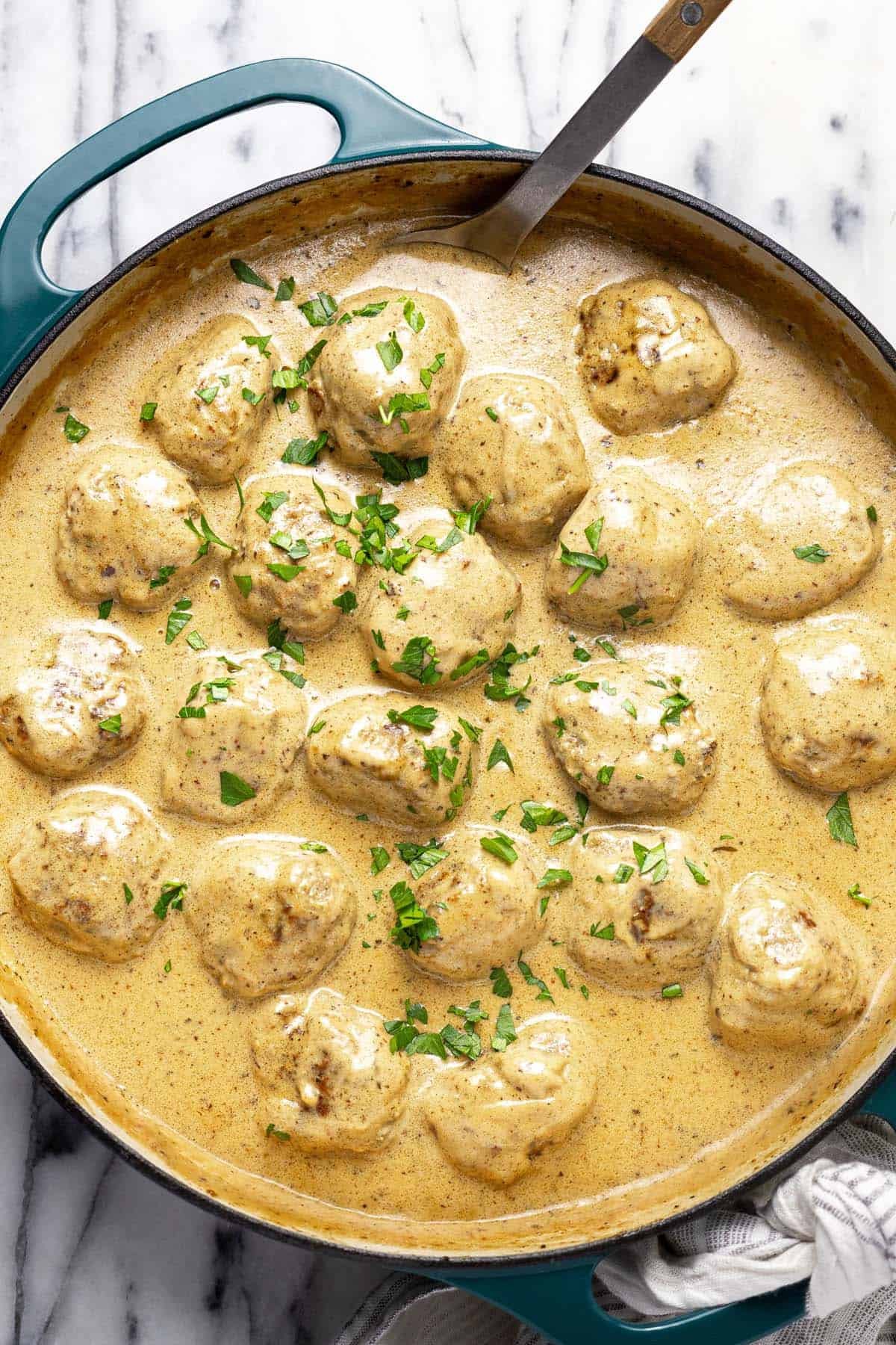 Large pan filled with creamy Swedish meatballs garnished with parsley.