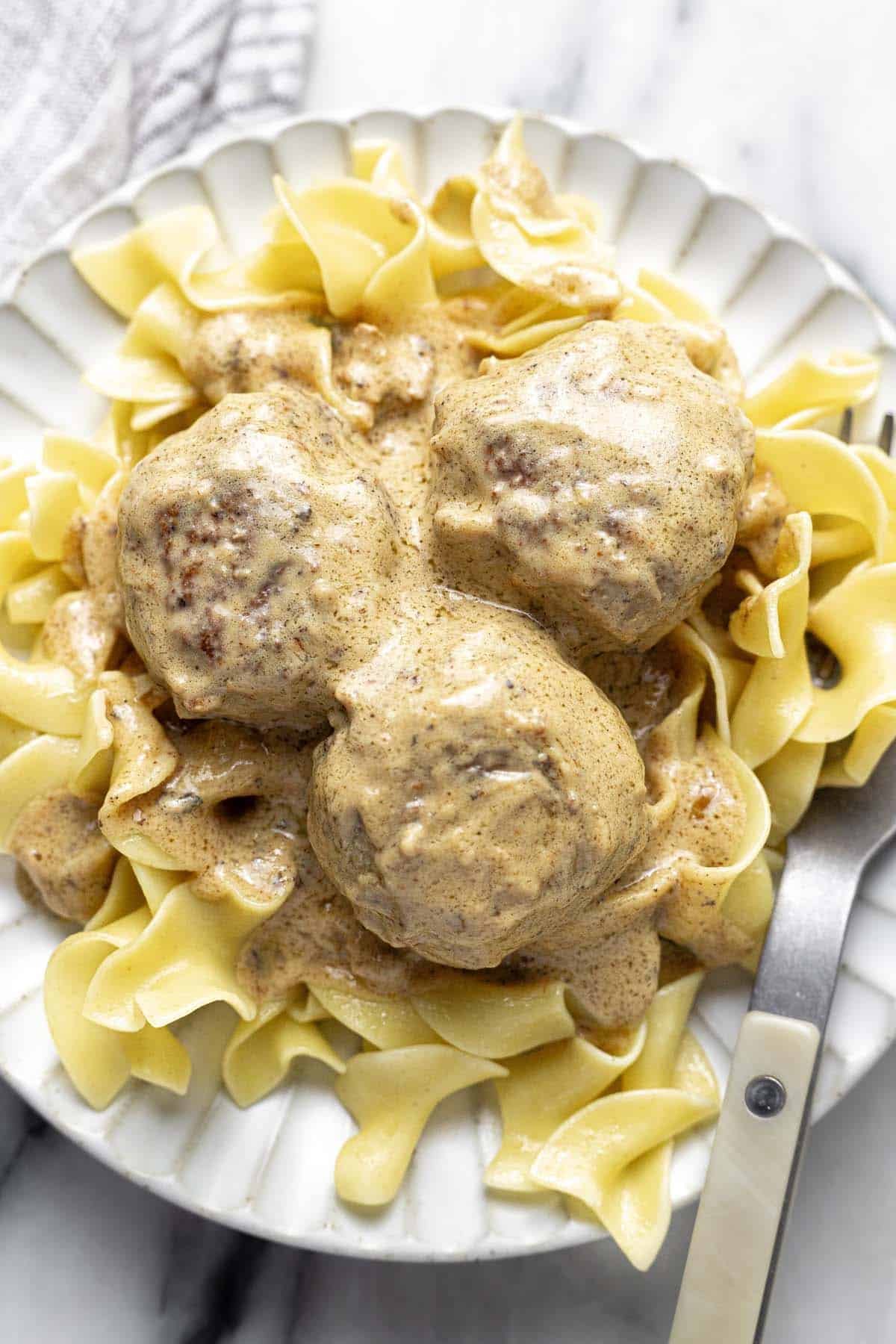 A plate of egg noodles topped with cream sauce and 3 Swedish meatballs.