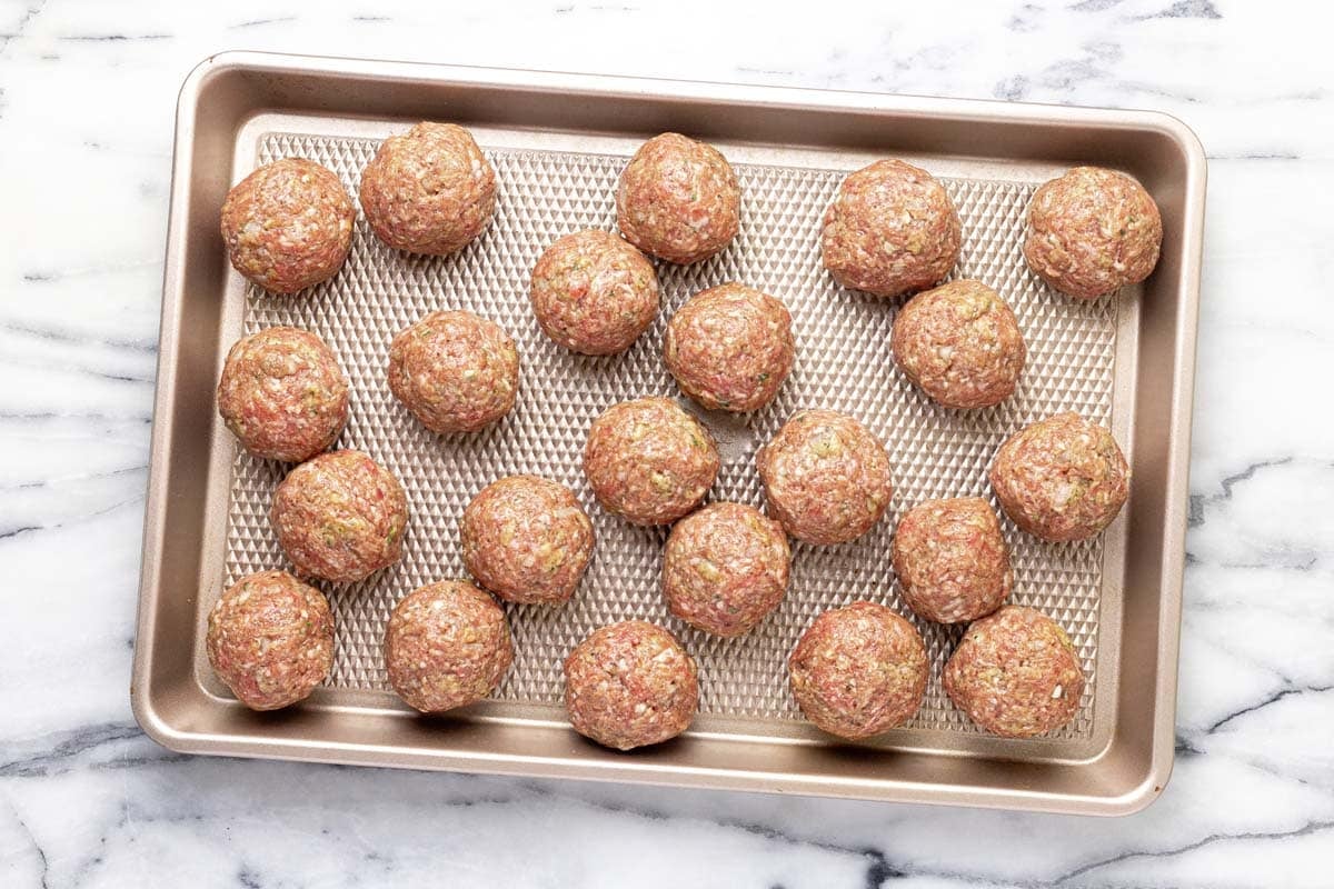 Freshly rolled meatballs on a large baking sheet.