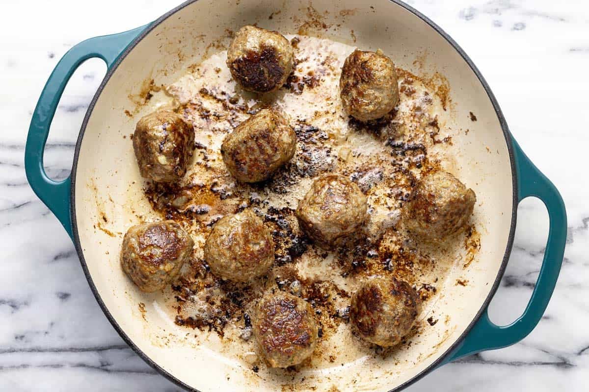 Seared meatballs in a large pan with oil.