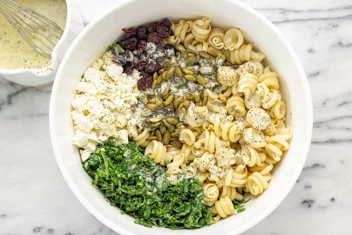 Bowl filled with pasta, cherries, feta, pumpkin seeds, and massaged kale with poppyseed dressing.