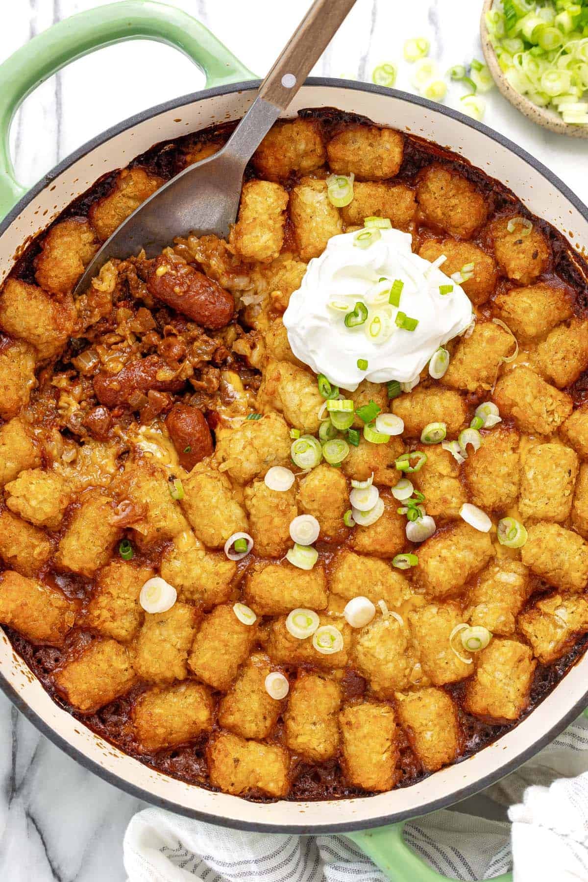 Large pan of chili cheese dog tater tot casserole topped with sour cream.