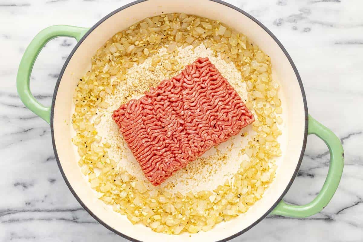 Pan with sauteed onion and garlic and raw ground beef in the middle.