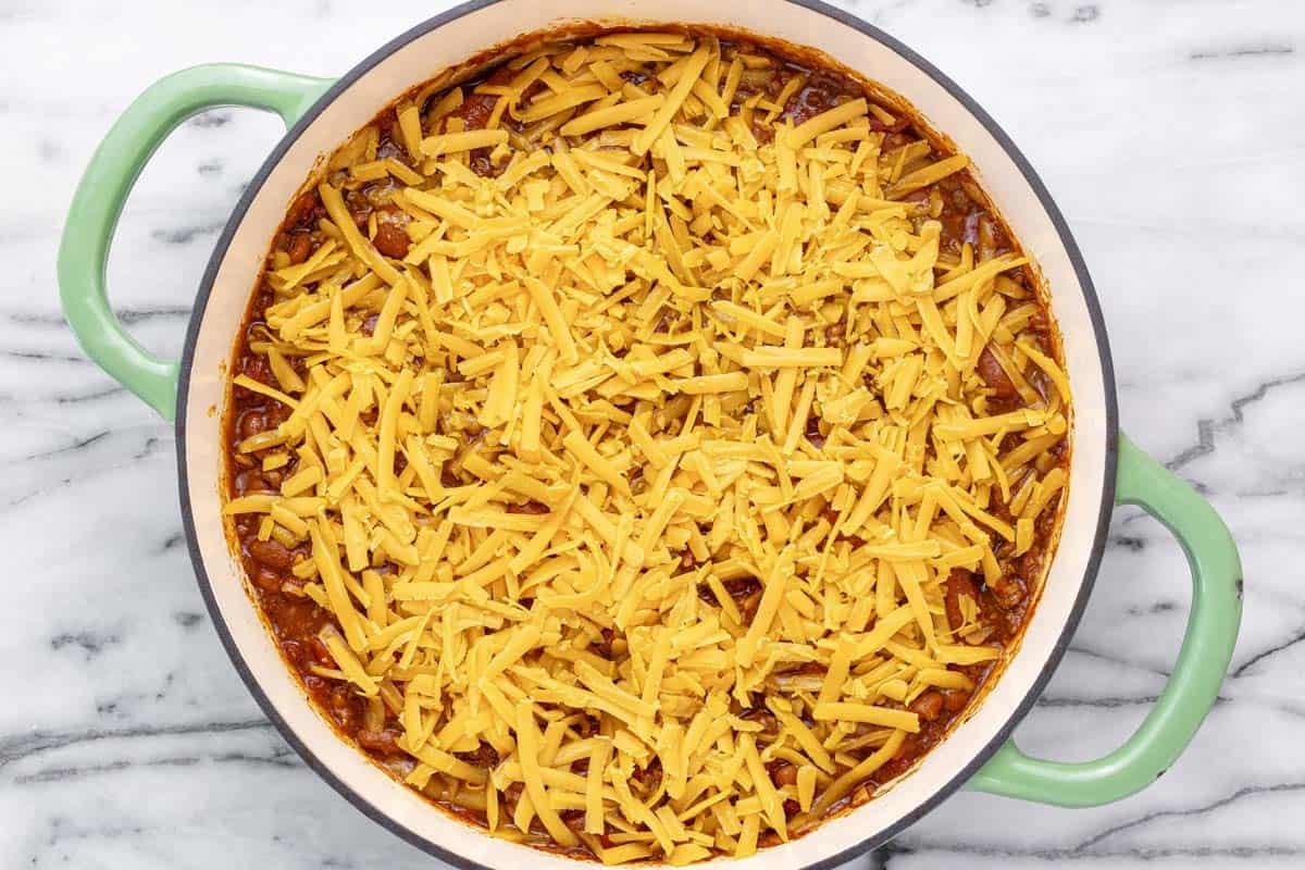 Shredded cheese on top of a pan of chili.