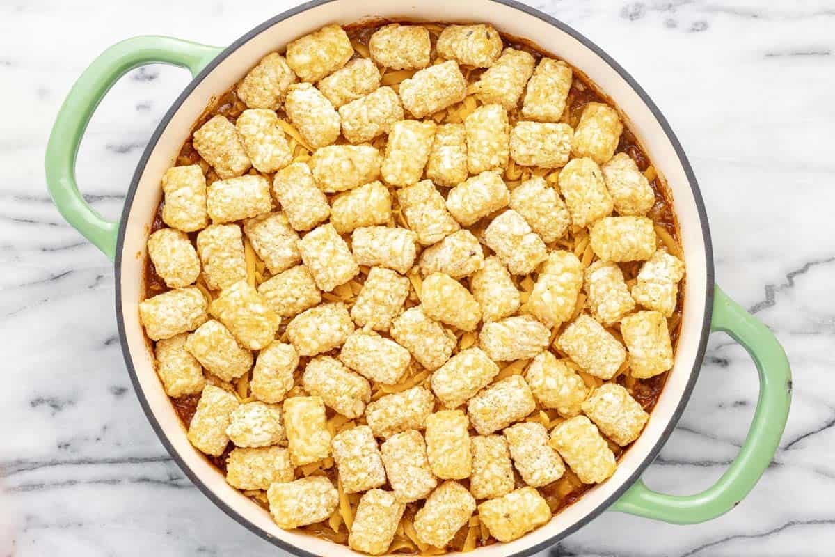 Frozen tater tots on top of cheese and chili in a pan.